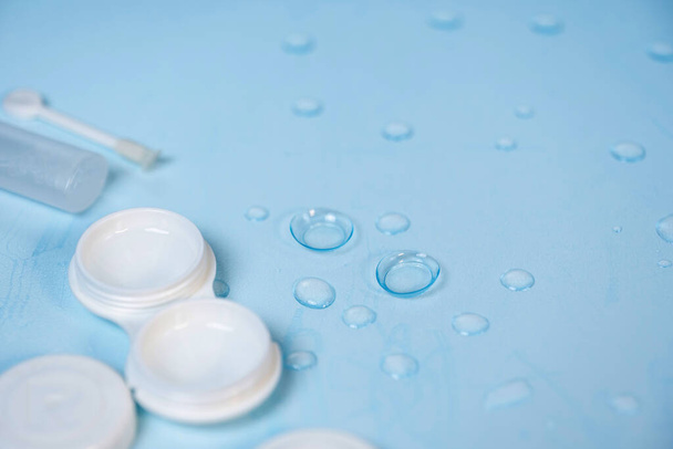 lentes de contato, estojo e ferramentas em um fundo azul com gotas de água - Foto, Imagem