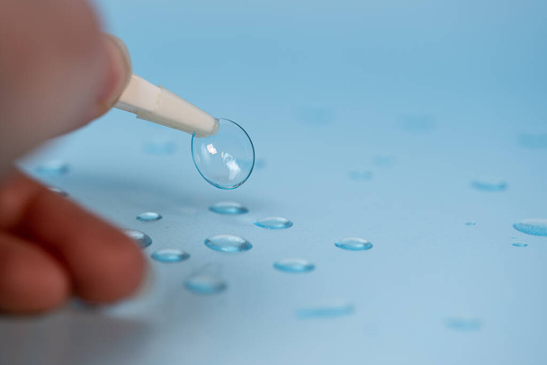on a blue background with water drops, a woman's hand takes the lens with tweezers - Photo, Image