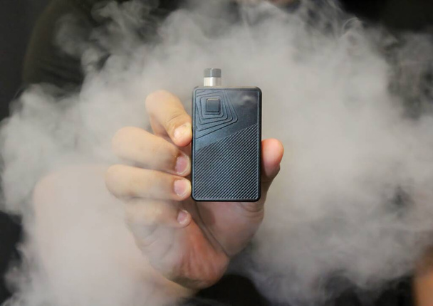 Male hand holding an e-cigarette vaping kit. Selective focus. Blurred background. - Photo, Image