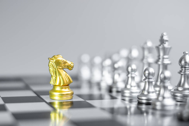 Złoty rycerz szachowy (koń) na szachownicy przeciwko przeciwnikowi lub wrogowi. Strategia, konflikt, zarządzanie, planowanie biznesowe, taktyka, polityka, komunikacja i koncepcja lidera - Zdjęcie, obraz