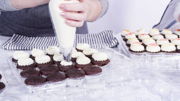 Stap voor stap. Piping Italiaanse boterroom glazuur op de top van mini chocolade cupcakes. - Foto, afbeelding