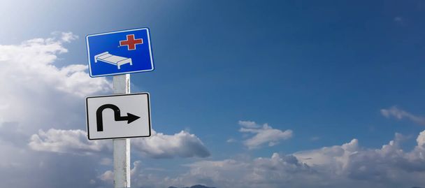 Verkehrszeichen, Krankenhaus voraus und Kehrtwende-Schilder am Mast isoliert auf trübem, blauem Hintergrund. - Foto, Bild