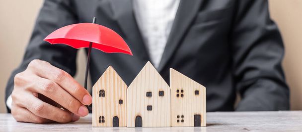 Empresario mano sosteniendo paraguas rojo cubierta de madera Modelo de casa en la oficina de la mesa. Seguros inmobiliarios y conceptos inmobiliarios - Foto, imagen