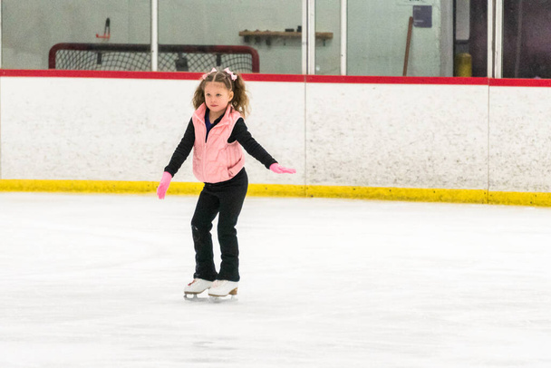 Κοριτσάκι εξάσκηση φιγούρα πατινάζ κινήσεις στο εσωτερικό παγοδρόμιο. - Φωτογραφία, εικόνα