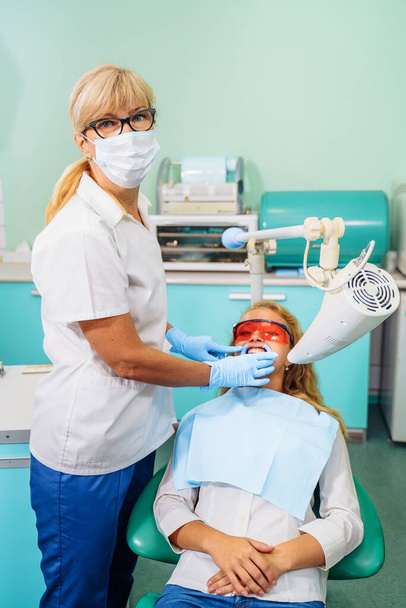 Blanqueamiento dental. Un paciente con gafas protectoras de los rayos en la silla del dentista. Examen preventivo de la cavidad oral. Instalando el espaciador bucal. En la cita con el dentista. - Foto, Imagen