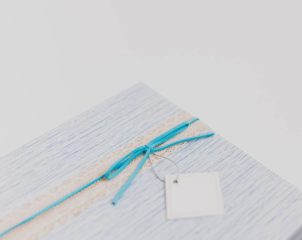 Fragment of blue gift present square box with suede bow and white blank card, low key pastel colors - 写真・画像