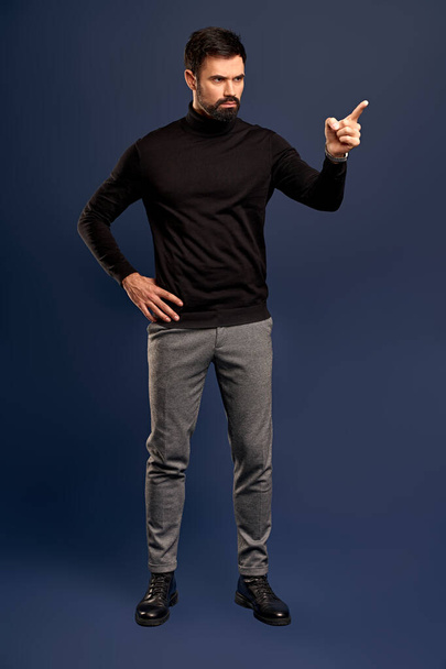 Young bearded stylish teacher or business man pointing finger side. Full body length portrait isolated on Pacific Blue studio background - Fotó, kép
