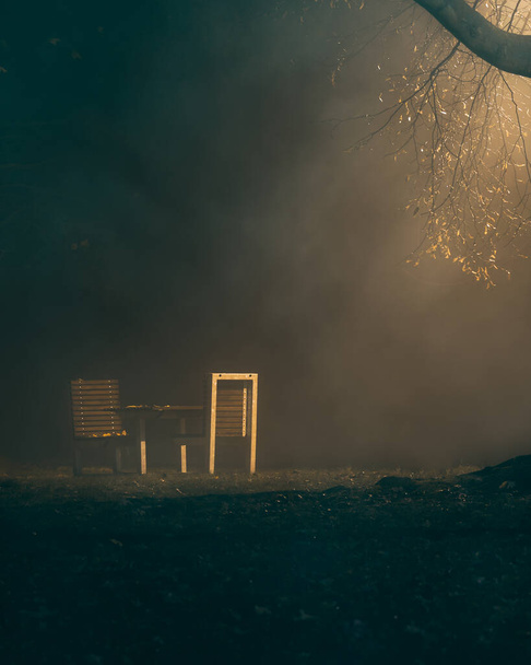 Bench a városi parkban ködbe burkolózva és utcai lámpákkal megvilágítva. Este, amikor leszáll a köd, ijesztő és titokzatos lehet.Ez a kép Csehországból származik, Vesel nad Lunic nevű kisvárosból.. - Fotó, kép