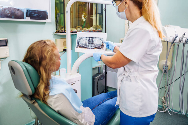 Hooggekwalificeerde tandarts biedt de patiënt effectieve oplossingen voor tandheelkundige problemen. Onderzoek van de mondholte aan de hand van het kaakbeeld. De dokter toont de patiënt een röntgenfoto.. - Foto, afbeelding