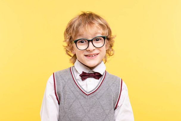 Portrait of cute 8-year-old boy with glasses on yellow background, frontal view. Beautiful, happy European school child. Smart child concept, back to school, glasses for vision. Horizontal, copy space - Foto, imagen