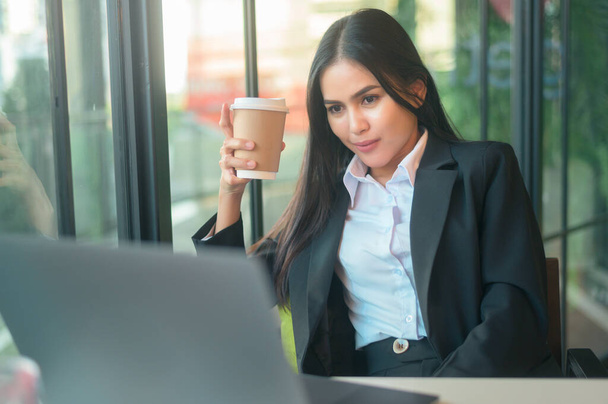 A beautiful business woman is analyzing financial data via computer , drinking coffee in coffee shop . business people lifestyle . technology concept . - Photo, Image