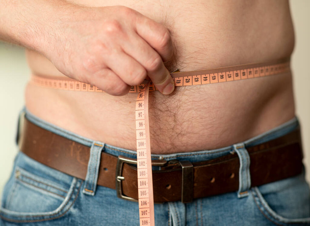 Gros plan de la mesure d'un ventre masculin avec un mètre de tailleur. L'homme montre son ventre nu - Photo, image