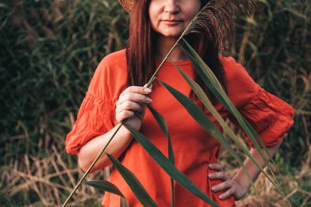 Portrait of a beautiful woman in a straw hat dressed in red clothes on a background of reeds and lake. Copy, empty space for text. - Photo, Image