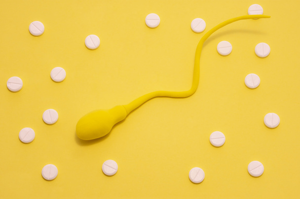Žlutý model spermií je na žlutém pozadí posetém puntíky z bílých pilulek. Koncepce diagnózy a léčby mužské neplodnosti a spermií - Fotografie, Obrázek