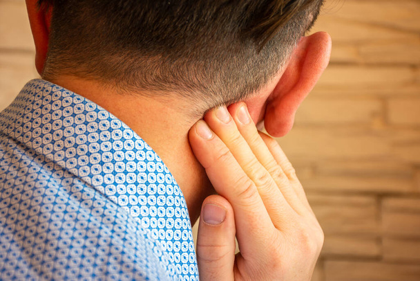 Dolor detrás de la oreja en el área de mastoides foto concepto de proceso. La persona sostiene su mano sobre el área detrás de la oreja, donde se sospecha de dolor debido a otitis media, inflamación, ruido en el oído, pérdida auditiva - Foto, Imagen