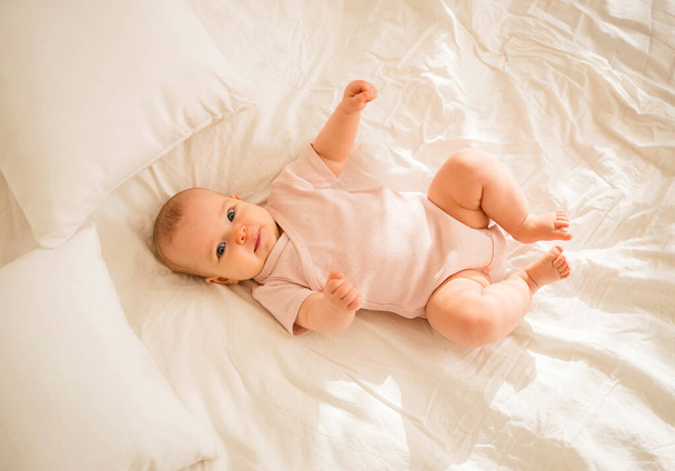 a little baby girl in a pink bodysuit is lying on the bed - Photo, Image