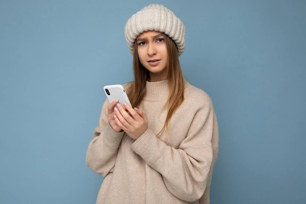 Zdjęcie atrakcyjne zdenerwowany niezadowolony przystojny młoda kobieta noszenie casual stylowy strój ustawienie izolowane na tle z pustej przestrzeni gospodarstwa w ręku i za pomocą wiadomości SMS telefonu komórkowego - Zdjęcie, obraz