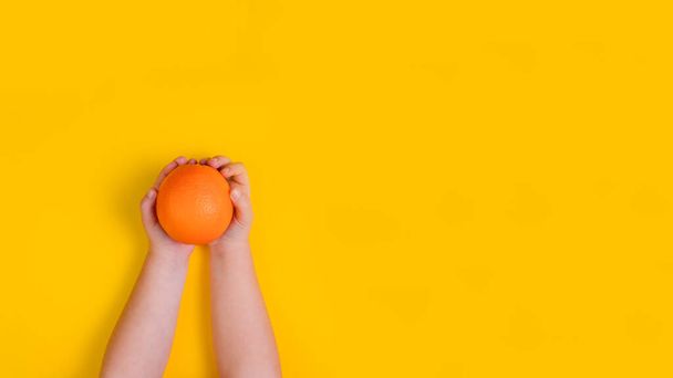 Hands of little girl with orange fruit on orange background. Top view. Banner. Copy space - Foto, Imagem