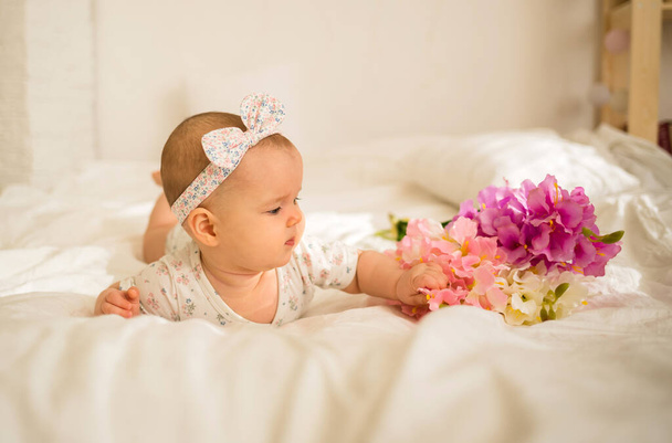 pieni tyttö kehonpuvussa makaa sängyllä ja katsoo kukkakimppua - Valokuva, kuva