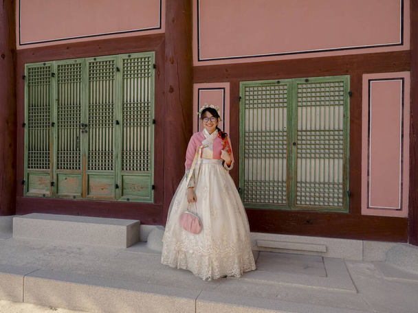 szczęśliwy azjatycki turysta kobieta w różowy koreański tradycyjny strój w historycznym starożytnym budynku - Zdjęcie, obraz