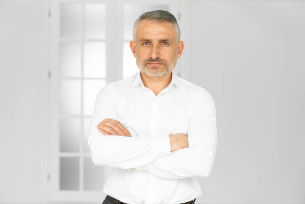 Sikeres idős férfi fehér ingben, hajtogatott kézzel, szürke háttér felett állva - Fotó, kép