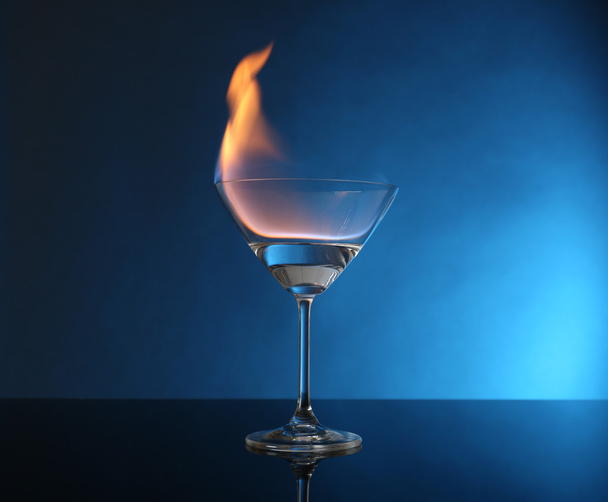 Glass with burning alcohol on blue background - Фото, изображение