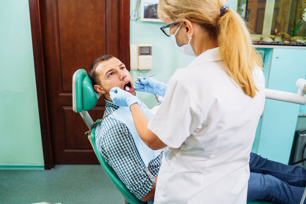 Diş kliniğinde ağzı açık bir hasta. Diş tedavisi için hazırlık. Tükürük, bor makinesi, diş aynası, cımbız ve diğer aletleri toplamak için pamuk kullanıyor. Tam zamanında tedavi önemlidir.. - Fotoğraf, Görsel
