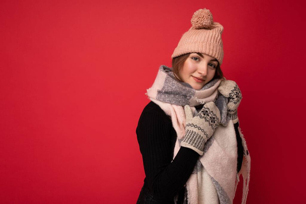 Photo of beautiful happy cute young brunette woman isolated over red background wall wearing winter scarf mittens and warm hat looking at camera and dreaming - Fotoğraf, Görsel