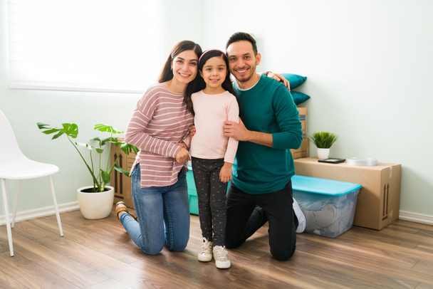Famille latine excitée et heureuse posant avec leur petite fille dans le salon de leur nouvelle maison après avoir emménagé et déballer - Photo, image