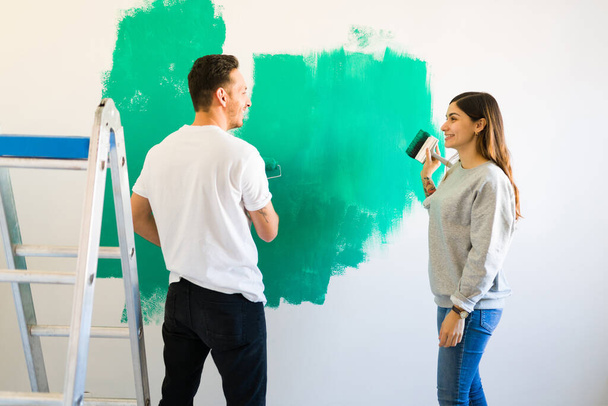 Szczęśliwa młoda kobieta i uśmiechnięty mężczyzna za pomocą pędzla i wałka do malowania zielonych ścian domu - Zdjęcie, obraz