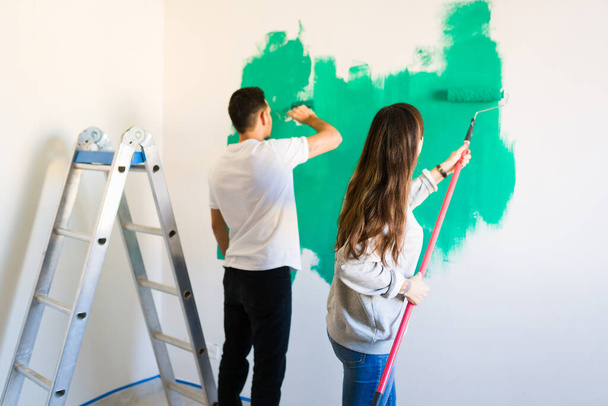 Freund und Freundin sehen, wie sie nach der Vermietung ihres neuen Hauses mit grüner Farbe die Wände streichen - Foto, Bild
