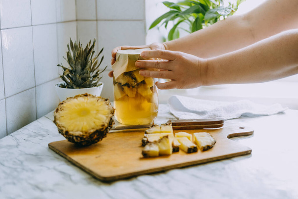 Erjesztett ananász kombucha ital tepache. Házi készítésű probiotikus szuperétel ananászos ital főzési folyamata. Igyál üveggel és szeletelt ananászt az otthoni konyhában. - Fotó, kép