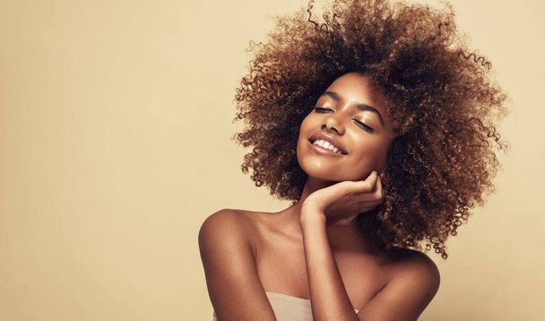 Beauty portrait of african american girl with clean healthy skin on beige background. Smiling dreamy beautiful black woman.Curly hair in afro style - Фото, зображення