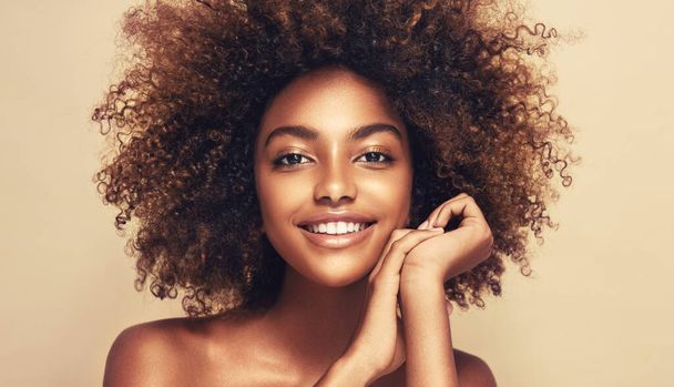 На бежевому тлі красивий портрет афро-американської дівчини з чистою здоровою шкірою. Посміхнена чорна жінка. Кучеряве волосся в африканському стилі. - Фото, зображення