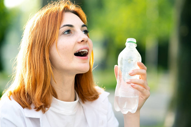 Jeune fille rousse heureuse tenant la bouteille d'eau dans ses mains dans le parc d'été. - Photo, image