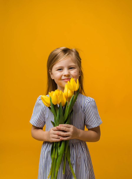 portret van een lachend meisje met een boeket gele tulpen op een gele achtergrond met ruimte voor tekst - Foto, afbeelding