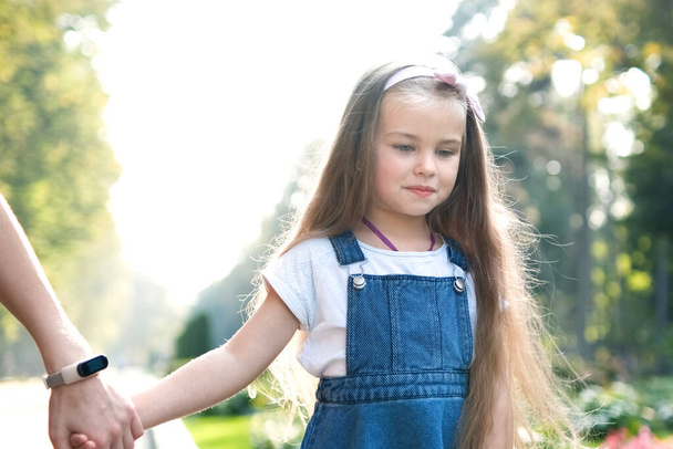 Young woman and her little daughter with long hair walking together holding hands in summer park. - Photo, Image