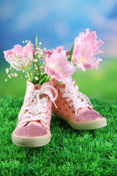 Beautiful gumshoes with flowers inside on green grass, on bright background - Foto, Imagen