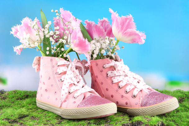 Hermosos zapatos de goma con flores en el interior sobre hierba verde, sobre fondo brillante
 - Foto, Imagen