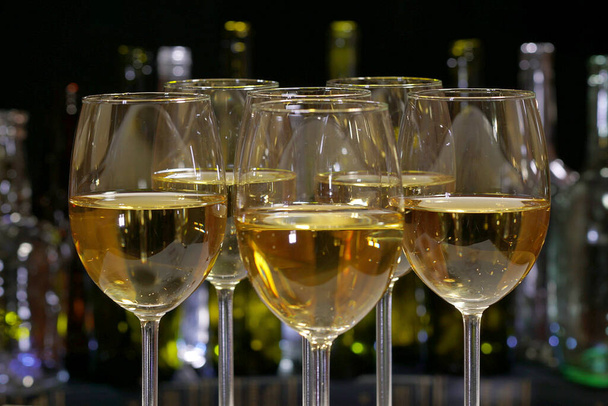 白ワイン。アルコールボトルの列を背景に白ワインとエレガントなワイングラス - 写真・画像
