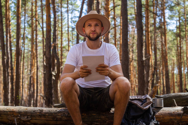 El hombre con sombrero tiene un mapa en sus manos durante un viaje de campamento. Caminata en las montañas, bosque. - Foto, imagen