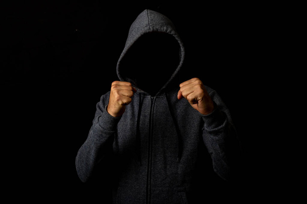 Hombre agresivo sin rostro en una postura de lucha en una capucha sobre un fondo oscuro. Añadido efecto de fallo. - Foto, Imagen