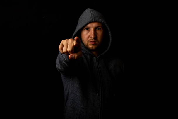Man in a hood points a finger against a dark background. - Photo, Image