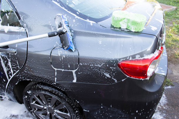 Konzept einer Autowaschanlage im Freien, bei der ein Auto mit einer Bürste mit Schaum gewaschen wird - Foto, Bild