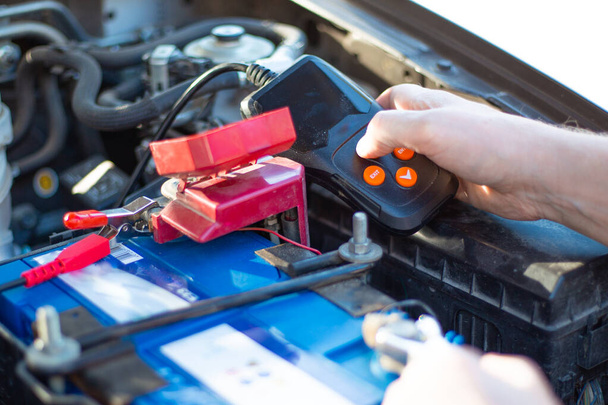 a car mechanic under the hood of a car diagnoses a car battery with a tester, close-up, repair and replacement of the battery - Foto, Imagem