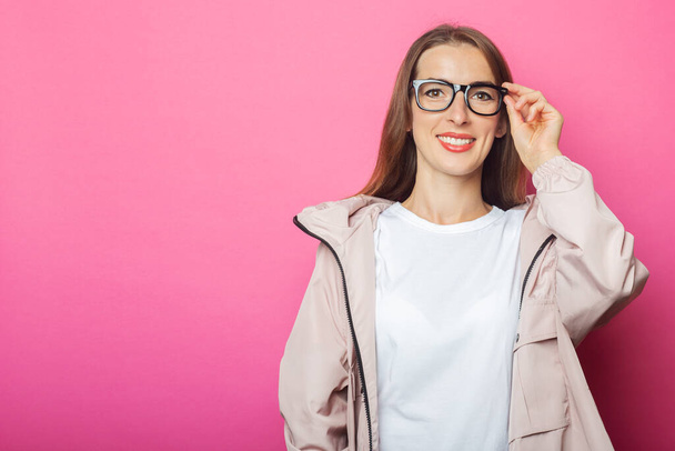 Young woman in glasses and pink jacket, pink isolated background. - Photo, Image