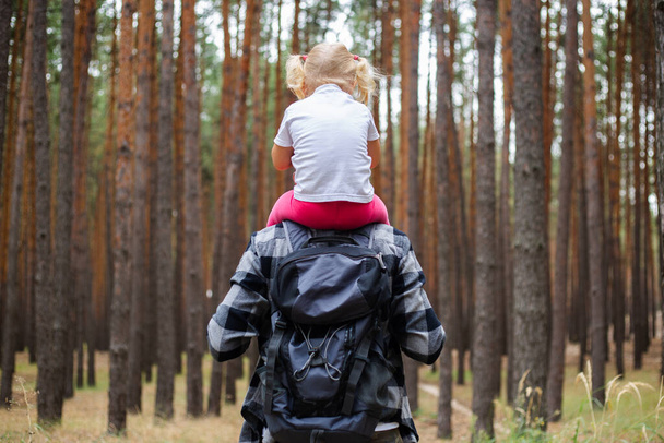 Man with a backpack carries a child on his shoulders in the forest. Family hike to the mountains or forest. - Foto, Imagem
