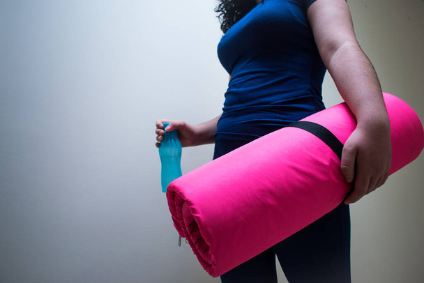 Nainen, jolla on vaaleanpunainen joogamatto ja sininen pullo käsissä valkoisilla taustoilla  - Valokuva, kuva