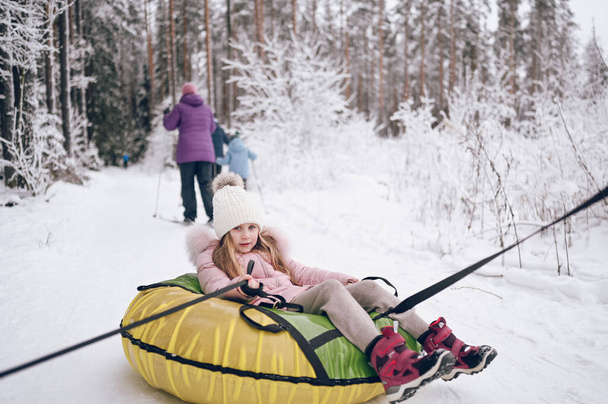 Malá roztomilá dívka v růžové teplé oblečení baví vyjížďky nafukovací sněhové trubice ve sněhobílé zimě venku. Rodinné sportovní rekreační aktivity - Fotografie, Obrázek