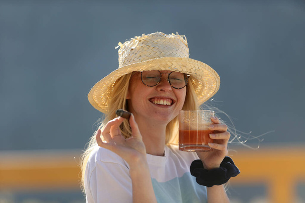 Une jeune femme avec un cigare et une tasse de boisson. Une fille avec un chapeau de beurre. - Photo, image